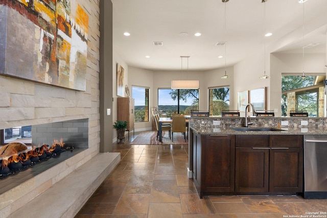 kitchen featuring light stone counters, dark brown cabinetry, a sink, dishwasher, and pendant lighting