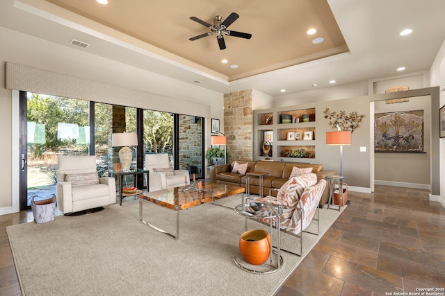 living area with a tray ceiling, stone tile flooring, visible vents, and baseboards