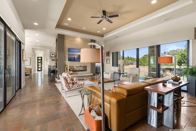 living room featuring stone tile floors, visible vents, a tray ceiling, a fireplace, and recessed lighting