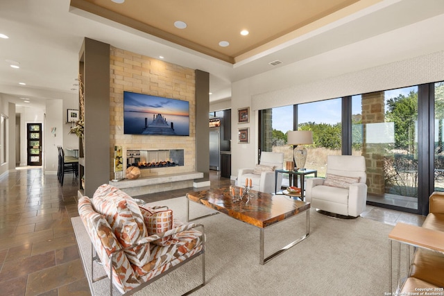 living room with recessed lighting, a multi sided fireplace, baseboards, a raised ceiling, and stone tile flooring