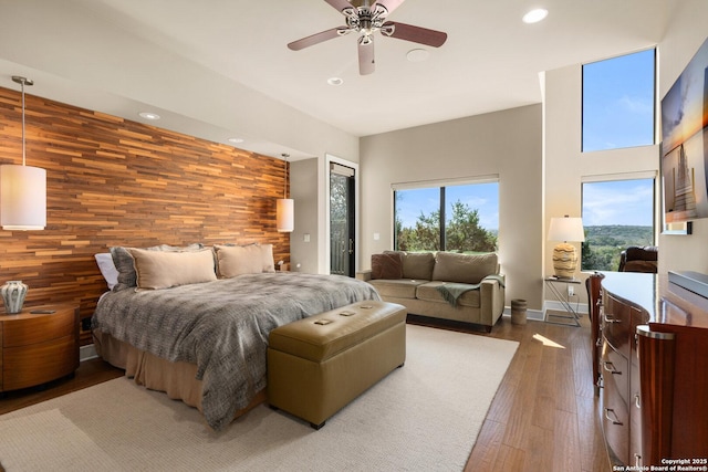 bedroom featuring an accent wall, dark wood-style flooring, multiple windows, and wood walls