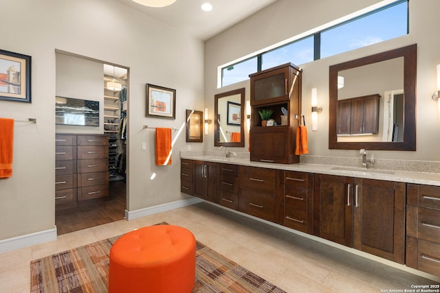 full bath featuring double vanity, a spacious closet, a sink, baseboards, and tile patterned floors