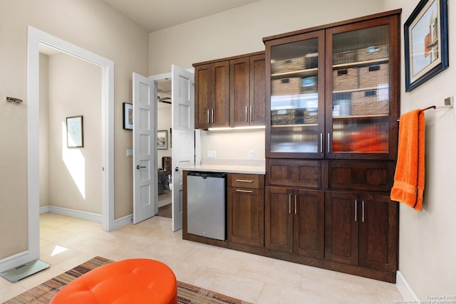 kitchen with light countertops, dark brown cabinetry, glass insert cabinets, and refrigerator