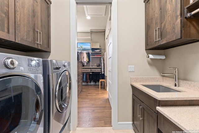 laundry room with a sink, baseboards, light wood-style floors, cabinet space, and washing machine and clothes dryer