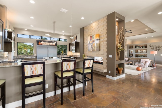 kitchen with hanging light fixtures, built in refrigerator, recessed lighting, and light stone countertops