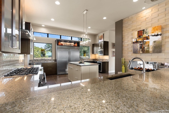 kitchen featuring built in appliances, dark brown cabinetry, a sink, a kitchen island, and pendant lighting