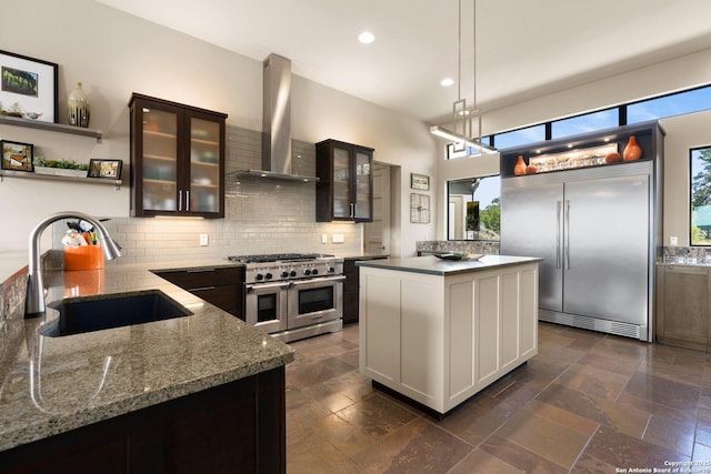 kitchen featuring premium appliances, wall chimney exhaust hood, glass insert cabinets, pendant lighting, and a sink