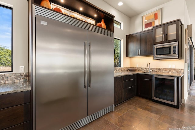 kitchen featuring built in appliances, beverage cooler, light stone counters, and plenty of natural light