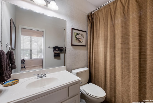 bathroom with toilet, vanity, and a textured wall