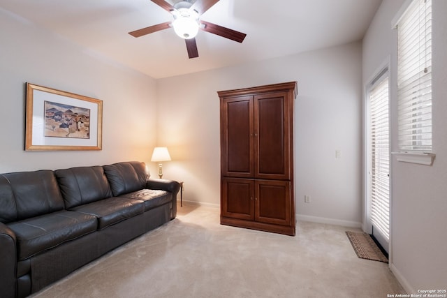 living area featuring light colored carpet, ceiling fan, and baseboards