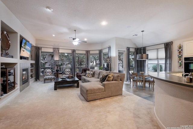 living room featuring lofted ceiling, ceiling fan, a tile fireplace, light carpet, and visible vents