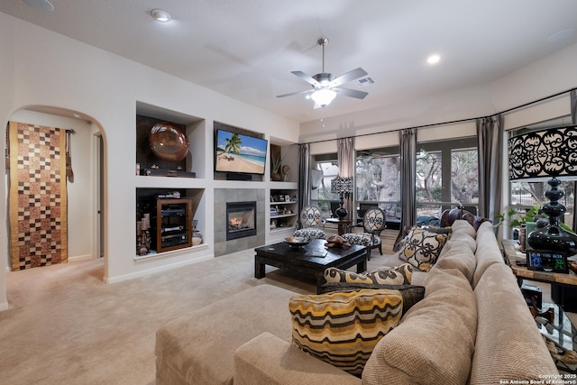 living room featuring ceiling fan, built in shelves, a tile fireplace, recessed lighting, and carpet