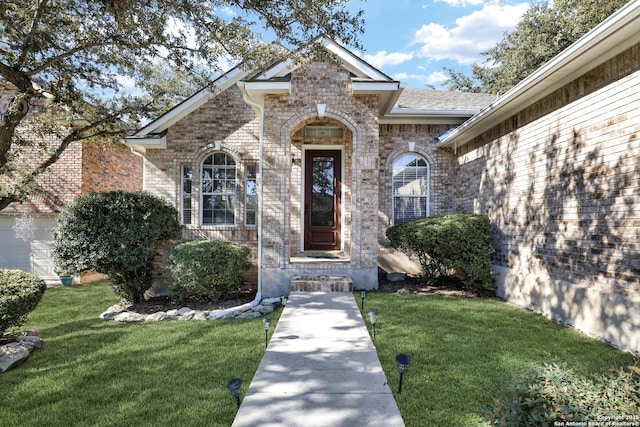 entrance to property with brick siding and a lawn