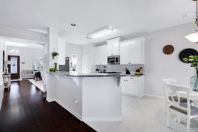 kitchen with tasteful backsplash, white cabinets, stainless steel microwave, a peninsula, and light stone countertops