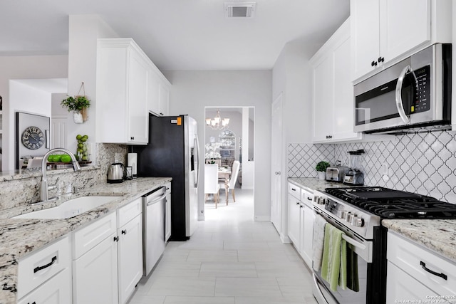 kitchen with light stone counters, stainless steel appliances, visible vents, white cabinets, and a sink