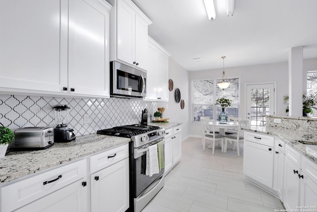 kitchen featuring appliances with stainless steel finishes, light stone counters, decorative light fixtures, white cabinetry, and backsplash