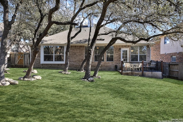 rear view of property with roof with shingles, brick siding, a lawn, and fence