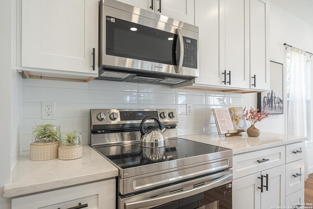 kitchen with stainless steel appliances, white cabinets, backsplash, and light stone countertops