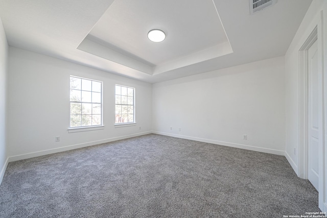 empty room featuring a tray ceiling, baseboards, visible vents, and carpet
