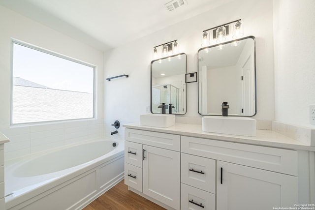 full bathroom featuring a bath, double vanity, a sink, and visible vents