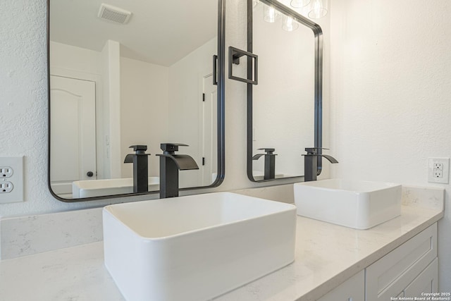 bathroom featuring a textured wall, double vanity, a sink, and visible vents