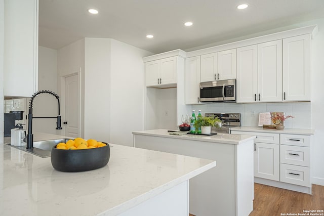 kitchen featuring appliances with stainless steel finishes, a center island, light stone countertops, white cabinetry, and backsplash