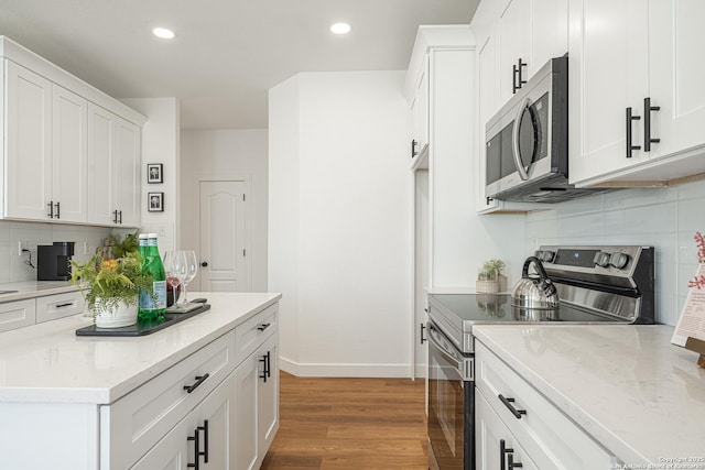 kitchen with stainless steel appliances, white cabinets, light stone counters, and wood finished floors