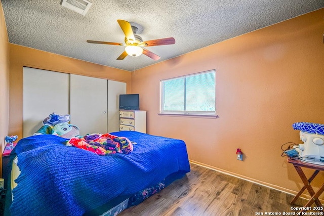 bedroom featuring baseboards, visible vents, wood finished floors, a textured ceiling, and a closet