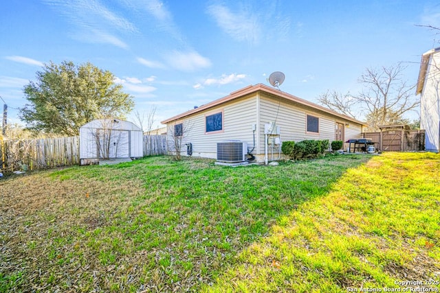 rear view of house with a yard, a storage unit, central AC unit, a fenced backyard, and an outdoor structure