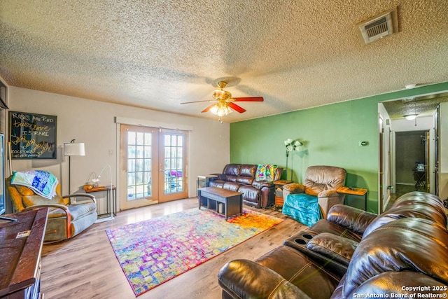 living room with light wood-style floors, ceiling fan, visible vents, and a textured ceiling