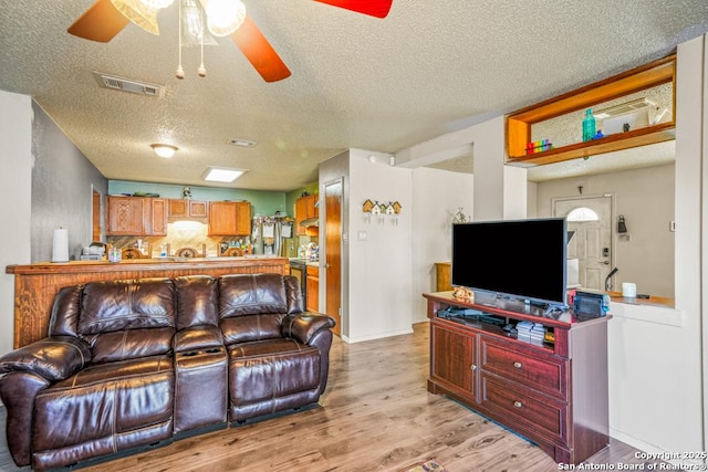 living room with light wood-style flooring, a textured ceiling, visible vents, and a ceiling fan