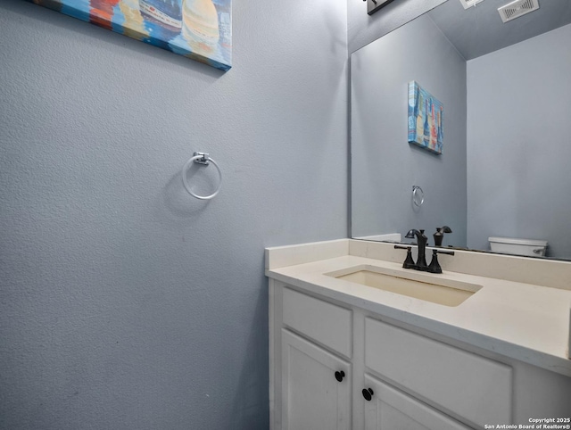 bathroom with toilet, vanity, and visible vents