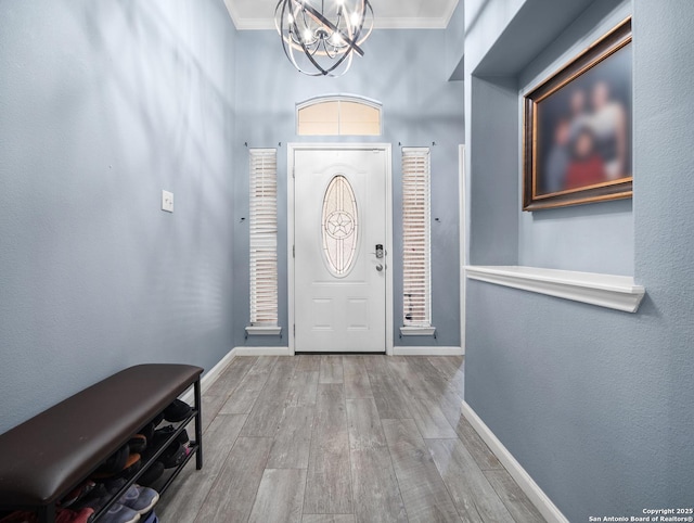 entryway featuring light wood-style floors, baseboards, crown molding, and an inviting chandelier