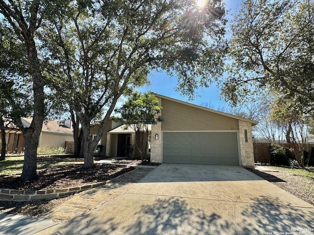 mid-century home with a garage, stone siding, fence, and concrete driveway