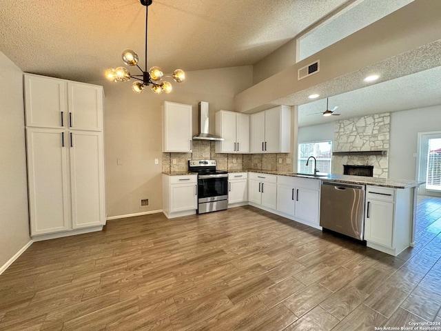 kitchen with white cabinetry, open floor plan, appliances with stainless steel finishes, wall chimney range hood, and decorative light fixtures