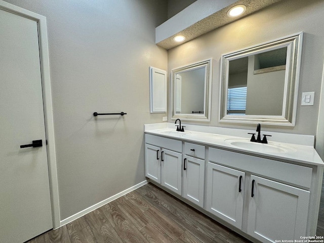 full bathroom with double vanity, baseboards, a sink, and wood finished floors