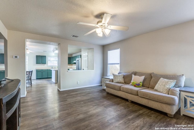 living area with ceiling fan, a textured ceiling, visible vents, baseboards, and dark wood-style floors