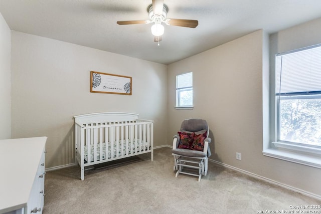 bedroom featuring a nursery area, a ceiling fan, and light colored carpet