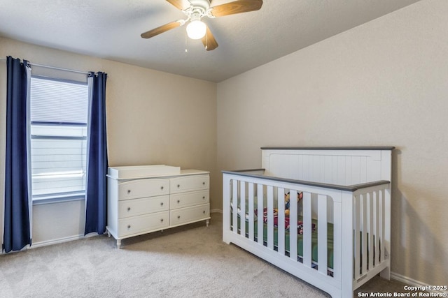 bedroom featuring a crib, baseboards, a ceiling fan, and light colored carpet