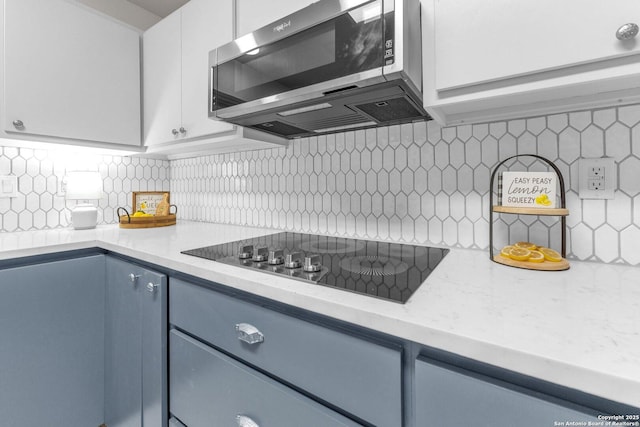 kitchen featuring tasteful backsplash, white cabinets, stainless steel microwave, light stone counters, and black electric stovetop