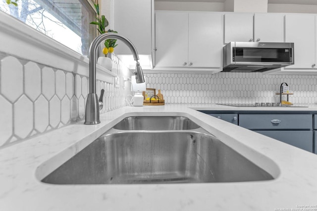 interior details with decorative backsplash, white cabinets, stainless steel microwave, light stone countertops, and a sink