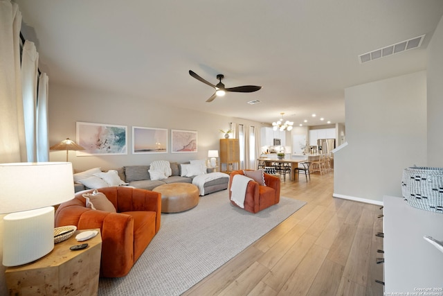 living room with ceiling fan with notable chandelier, visible vents, and light wood-style floors