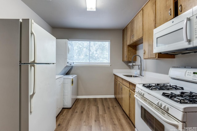 kitchen with light countertops, brown cabinetry, a sink, light wood-type flooring, and white appliances