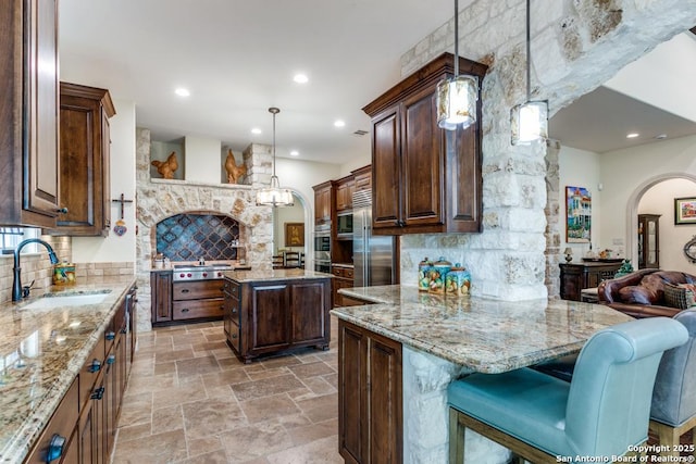 kitchen with arched walkways, a kitchen breakfast bar, a center island, pendant lighting, and a sink