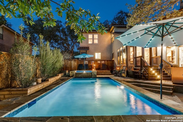 pool at twilight with fence, an outdoor pool, a patio, and an in ground hot tub