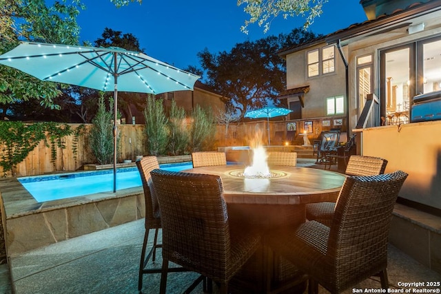 patio at twilight with fence, an outdoor pool, a fire pit, and exterior bar