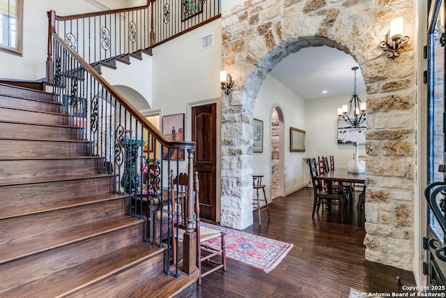 entrance foyer featuring arched walkways, dark wood-style flooring, visible vents, a towering ceiling, and a chandelier