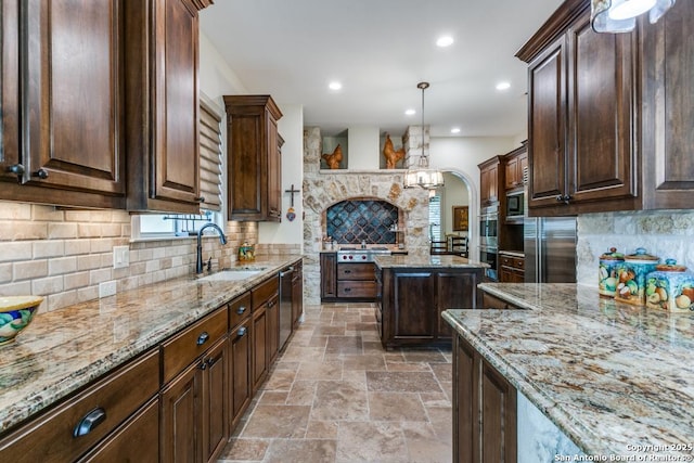 kitchen featuring light stone counters, stainless steel appliances, hanging light fixtures, a sink, and dark brown cabinets