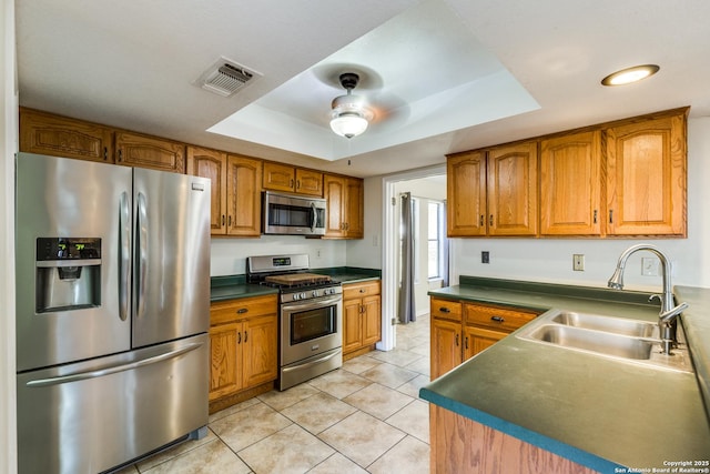 kitchen featuring visible vents, brown cabinets, a tray ceiling, stainless steel appliances, and a sink