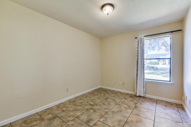 spare room with a textured ceiling, baseboards, and light tile patterned floors